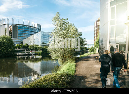 Strasbourg, France - May 19, 2017: Couple walking admiring the headquarter of European Parliament in Strasbourg with calm flowing Ill river and passerelle to the old building Stock Photo