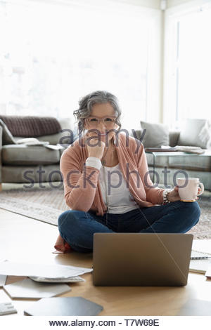 Portrait happy senior woman working from home, using laptop on floor