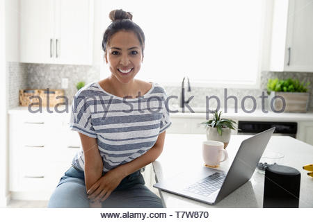 Portrait confident woman working from home at laptop in kitchen