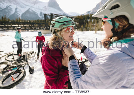 Woman fastening friend's helmet, preparing to fat bike in snow