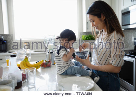 Mother and toddler daughter eating blueberries in kitchen
