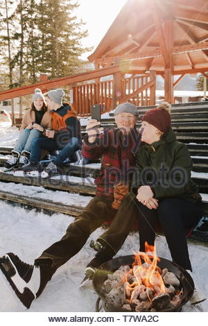 Senior couple in ice skates taking selfie on snowy steps by fire