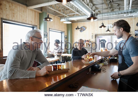 Male bartender serving beer tasting flights to customers in brewhouse