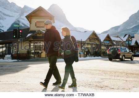 Senior couple walking on sunny, snowy street in mountain town
