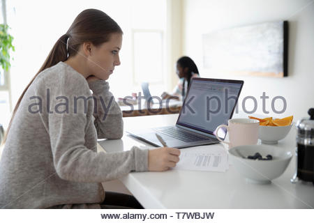 Young woman working from home, using laptop in kitchen