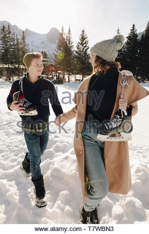 Young couple with ice skates holding hands, walking in snow