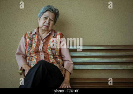 bored depressed asian elder woman sitting on bench. elderly female feeling sad lonely. senior lifestyle Stock Photo
