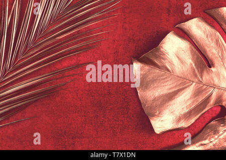 Closeup of golden palm and monstera leaves on abstract red textured background. Tropical conceptual elegant trendy summer background. Flat lay. Copy s Stock Photo