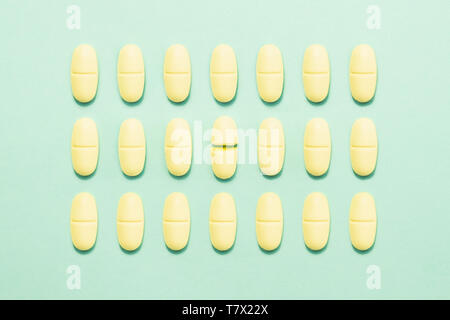 Medicine pill broken in half among whole tablets on geen background. Concept of emotional burnout, mental health or improper medical treatment Stock Photo