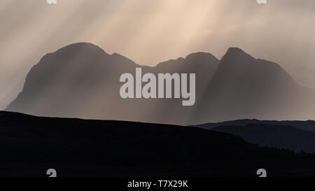 Sun rays, also called crepuscular rays, streaming through gaps in clouds above the iconic mountian of Suilven in Assynt in the far north of Scotland Stock Photo
