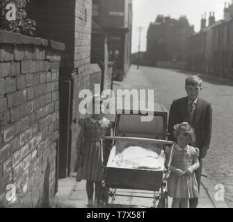 1950s, historical, young boy with his two little sisters and a baby in a pram pose for a picture standing on the pavement in the street, Manchester, England, UK. Stock Photo