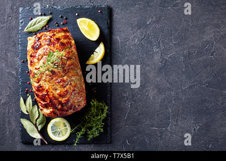 baked chicken meatloaf on a slate tray with lemon slices and fresh thyme on a concrete table, view from above, flat lay, copy space Stock Photo