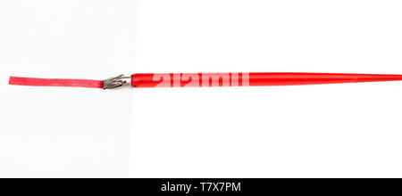 side view of red dip pen drawing a red line on sheet of paper by wide nib isolated on white background Stock Photo