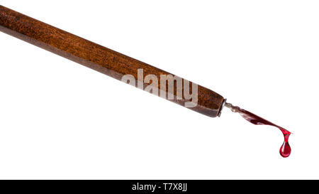 side view of red ink drop dripping from tip of nib of brown dip pen close up isolated on white background Stock Photo