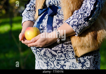 pregnant woman in blue dress holds a round yellow apple Stock Photo