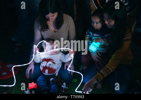 Mother and baby sensory play group are using LED lighting and toys for developmental play. Stock Photo