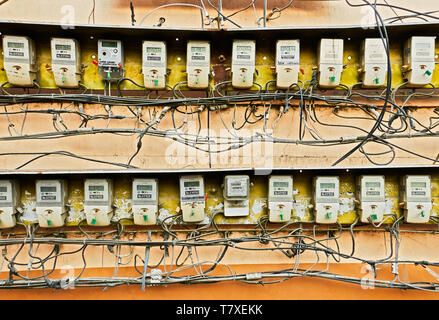 Leon, Iloilo Province, Philippines - April 18, 2019: Many electric power meters in line attached to a panel on a wall with many cables in disorder Stock Photo