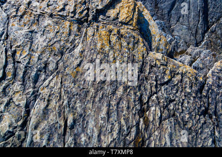 Close up of Welsh slate worn smooth by flowing water with patches of orange and yellow lichen. Stock Photo