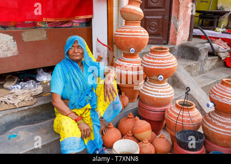 Street scene, Mahipalpur district, a New Delhi suburb: a local old woman sits on the pavement outside a shop with a display of ceramic pots Stock Photo