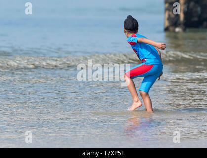 Young boy wearing a turban paddling in the sea in Spring in Brighton, East Sussex, England, UK. Child with turban. Presumably a Sikh. Stock Photo