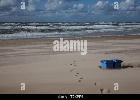 footprints and rather burried trash cans on the beach in sunshine Stock Photo