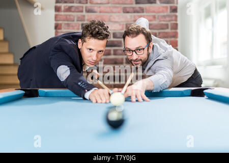 Two fashionable men friends aiming white billiard game pool ball. Stock Photo