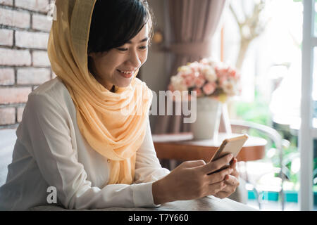 muslim woman using mobile phone at home sitting Stock Photo