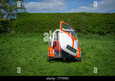 An orange and white two tone classic BMW Isetta bubble car with the single front door part open. Stock Photo