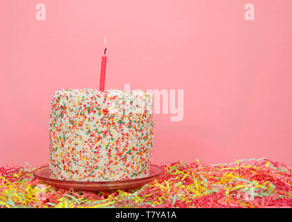 Fairy rainbow candy sprinkles cake on pink pedestal with colorful confetti below, simple pink background. One pink candle burning brightly. Mother's D Stock Photo