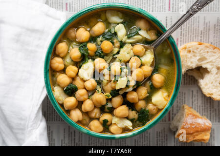 Chickpea soup with spinach and dry salted cod in a rustic bowl on a newspaper background Stock Photo