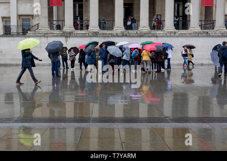 During seasonal rain, reflections of visitors and their umbrellas on the pavement of Trafalgar Square, on 9th May 2019, in London, England. Stock Photo