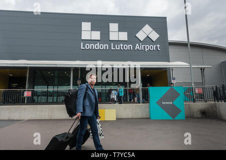 London Luton Airport new terminal building logo with male caucasian traveller wearing a rucksack and pulling two suitcases with his tongue out Stock Photo