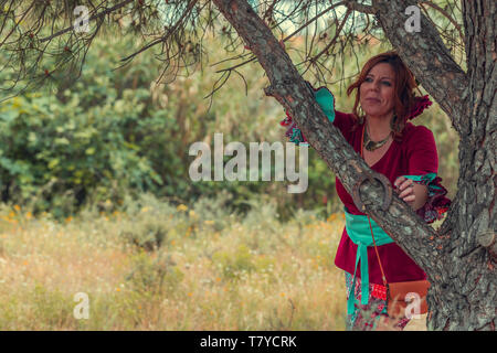 Woman in traditional rociero dress resting on an pine tree resting with nature in the background Stock Photo