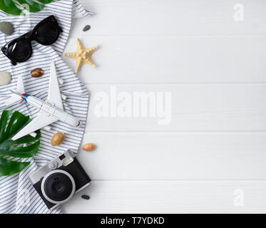 Time to travel concept. Camera, plane, sunglasses, monstera leavs, plane, star fish and towel on white wooden table. Vacation background flat lay with Stock Photo