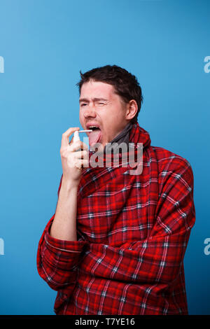 A wrapped in a blanket sick man is using spray with medicine for throat. Stock Photo
