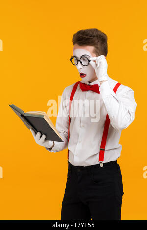 portrait of mime man artist reading book isolated on yellow background Stock Photo