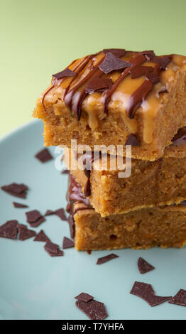 Stack of three sweet potato blondies with thin lines of chocolate and caramel icing running down at the sides and chocolate chips on teal plate, green Stock Photo