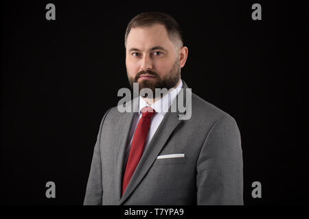 Portrait of Attractive bearded business man wearing at suit and red tie in front of a black background Stock Photo