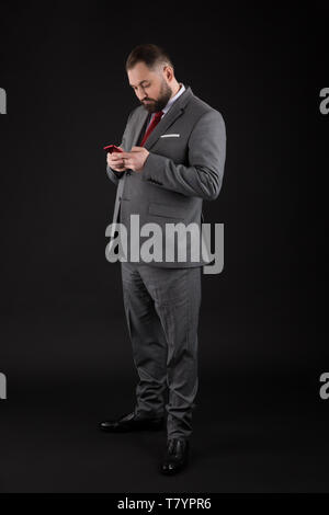 Businessman well groomed man hold smartphone. Man wearing at formal suit use smartphone social networks. Guy surfing internet smartphone black backgro Stock Photo