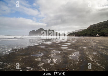 Bethells beach or Te Henga in Waitakere, West Auckland on a winters day with blue sky and white clouds. Low tide and relatively calm sea. Stock Photo