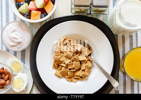 A bowl of cereal as part of a balanced breakfast.  Includes:  Yogurt, almonds, hard boiled egg, mixed fruit, orange juice, and milk.  Flat lay, over h Stock Photo