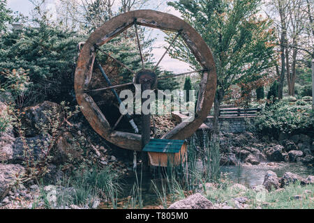 Water wooden old wheel mill in country village near pond stream. Retro vintage machinery in idyllic rustic rural country-side. Stock Photo