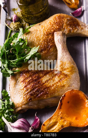 Grilled chicken legs served with roasted pumpkin, pesto sauce and fresh parsley on rustic wooden table, meat and vegetables roast dinner Stock Photo