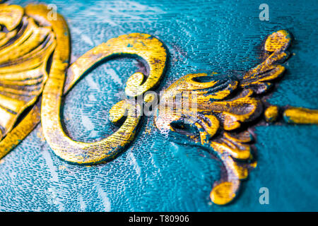 Vintage furniture details close up. Luxurious, floral decorations carved in wood, painted in bright grungy yellow on a blue wooden furniture cabinet. Stock Photo