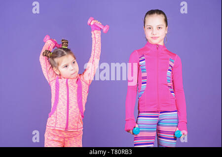 Following her sister. Girls cute kid exercising with dumbbells. Motivation and sport example concept. Toddler repeat exercise after sister. Sport exercises for kids. Healthy upbringing. Sporty babies. Stock Photo