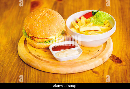 Burger menu. High calorie snack. Hamburger and french fries and tomato sauce on wooden board. Fast food concept. Burger with cheese meat and salad. Cheat meal. Delicious burger with sesame seeds. Stock Photo