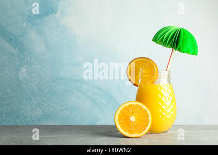 Glass jar with fresh orange juice, decorative palm and oranges on grey table against color background, space for text. Fresh natural drink Stock Photo