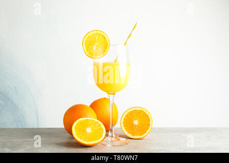 Glass with fresh orange juice and tubule, oranges on grey table against color background, space for text. Fresh natural drink Stock Photo
