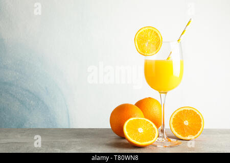 Glass with fresh orange juice and tubule, oranges on grey table against color background, space for text. Fresh natural drink Stock Photo