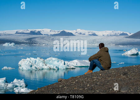 Young male sat admiring the view of Jokulsarlon Glacier Lagoon, South East Iceland, Iceland, Polar Regions Stock Photo
